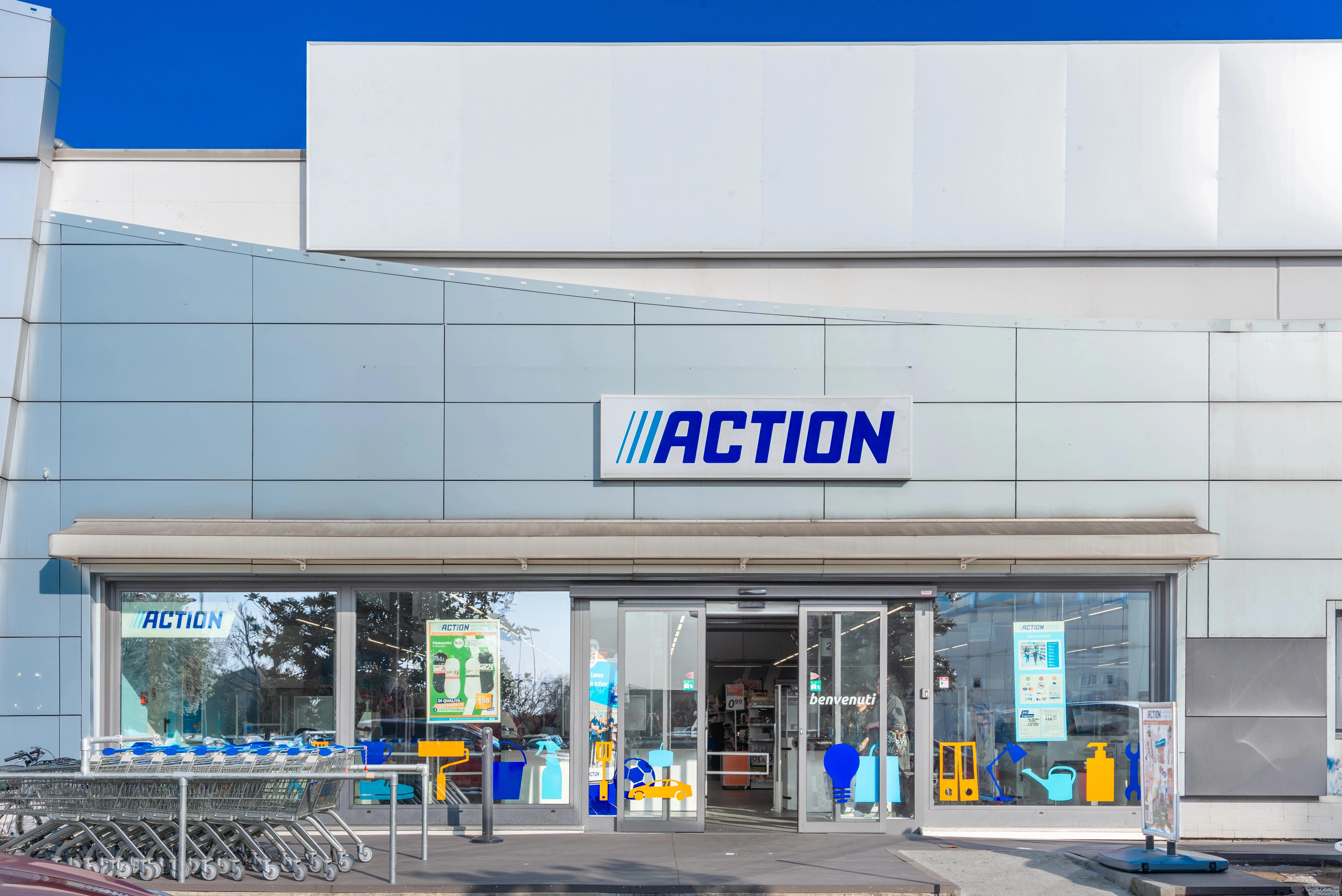 Vstupní část obchodu Action s logem, skleněnými dveřmi a řadou nákupních vozíků