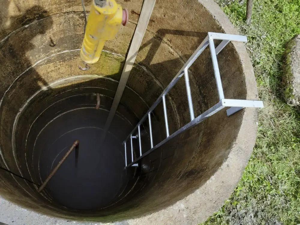 Ruka nabírající vodu ze studny do sklenice, v pozadí přírodní scenérie