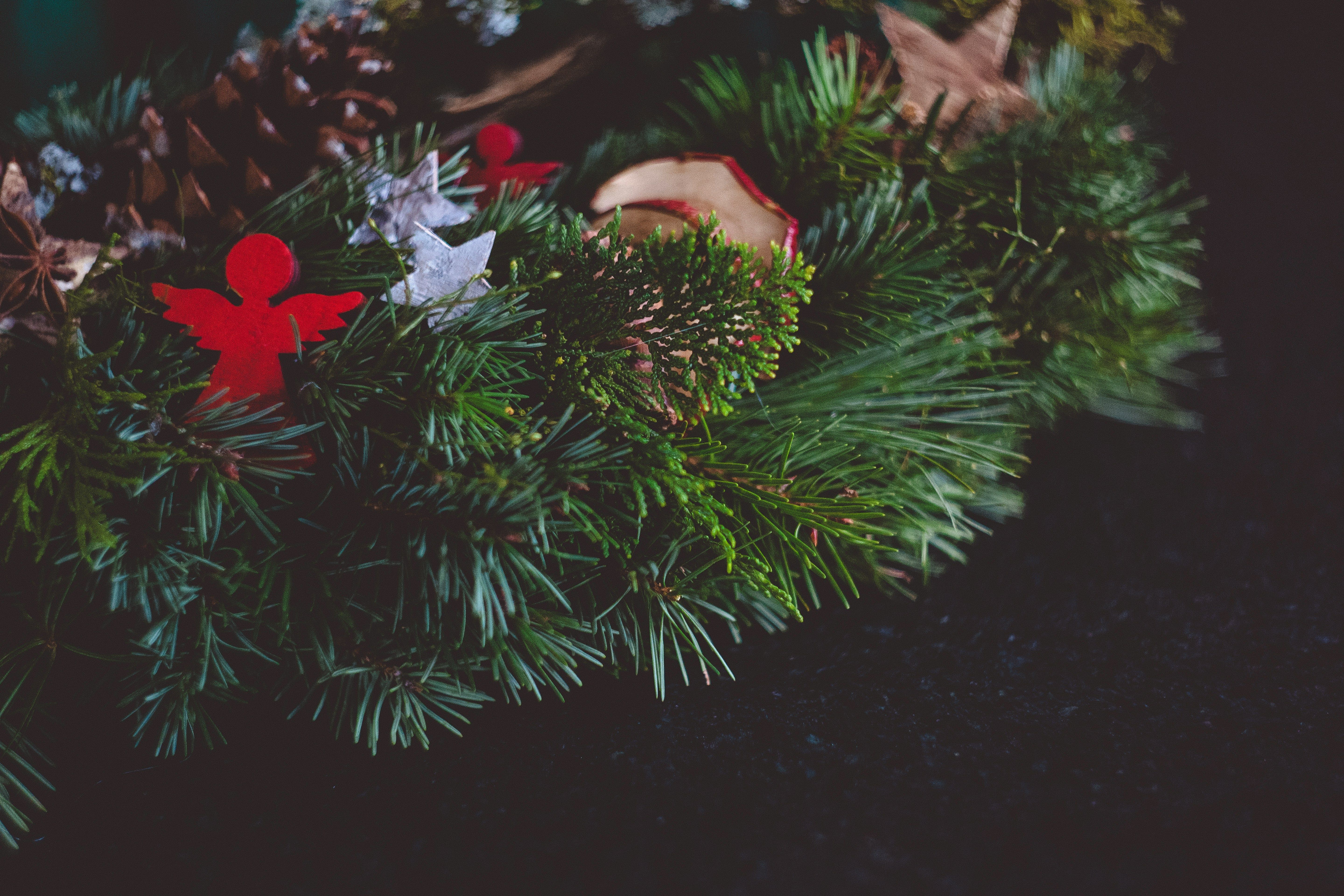 Ručně vyrobený adventní věnec ozdobený smrkovými větvemi, šiškami a červenými ozdobami ve tvaru andílka