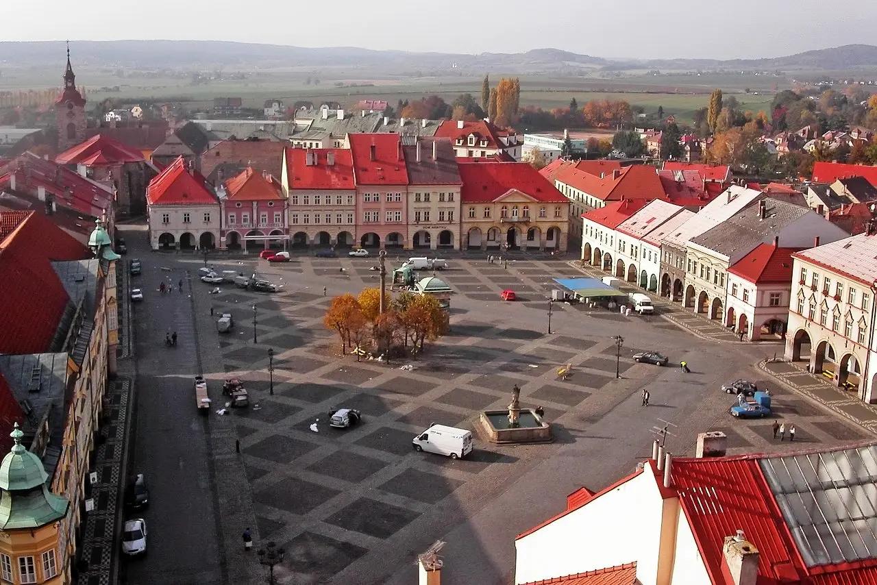 Lidé procházející se po náměstí v Jičíně s kavárnami a obchody