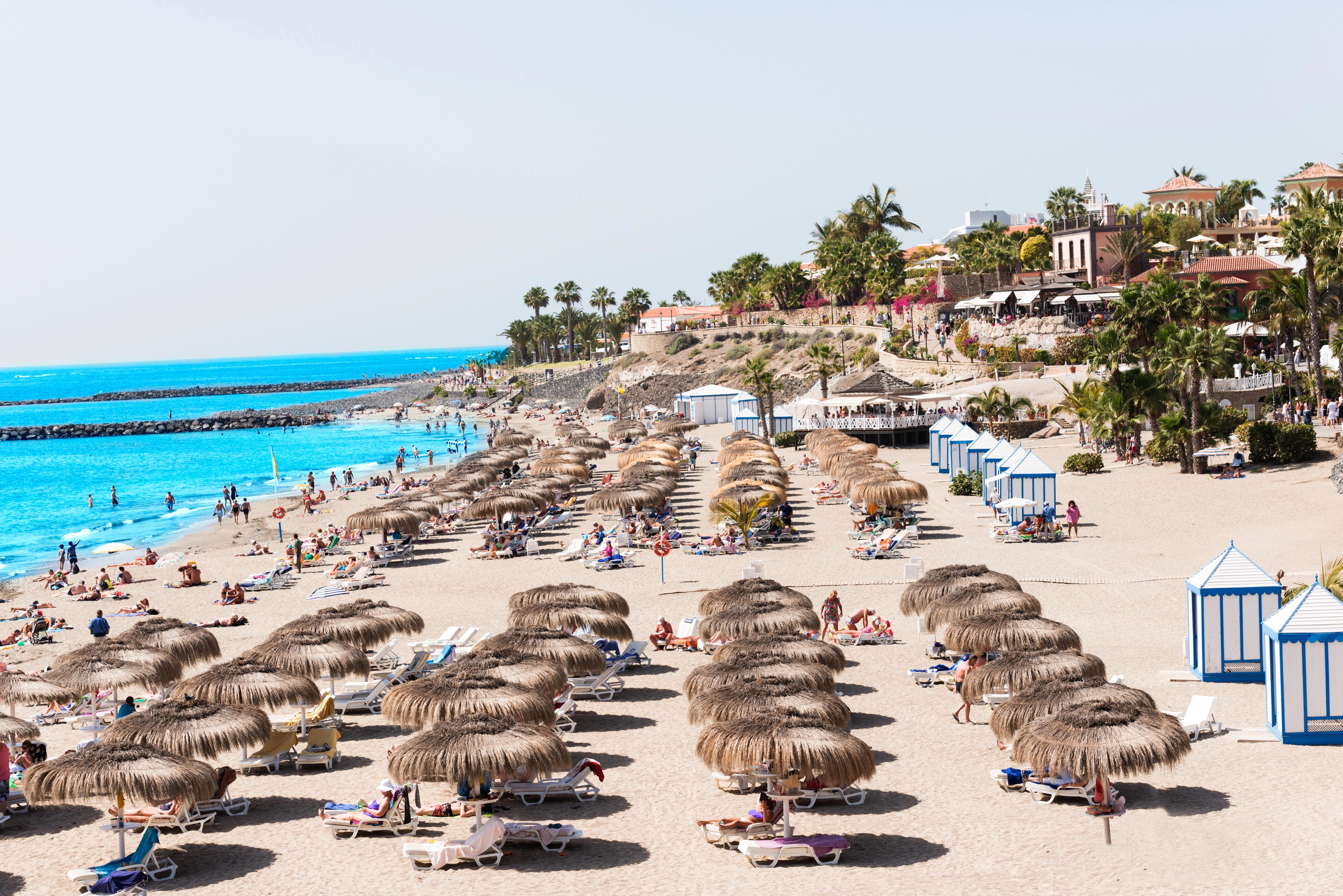 Slunná pláž Playa del Duque na Tenerife s řadami slunečníků a modrobílými kabinkami