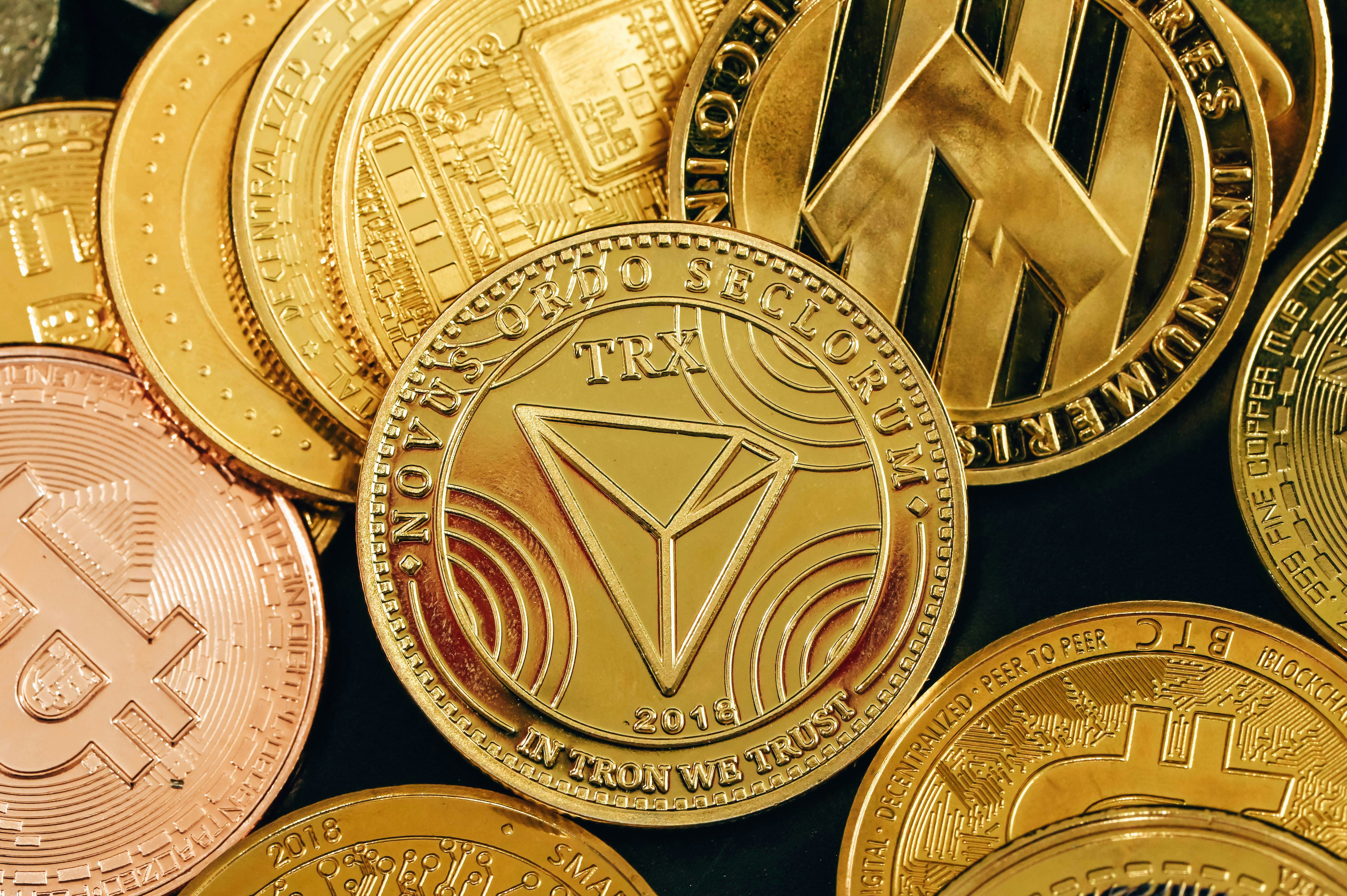 Detailní záběr na různé kryptoměnové mince, včetně symbolů pro Bitcoin, Tron a další.
