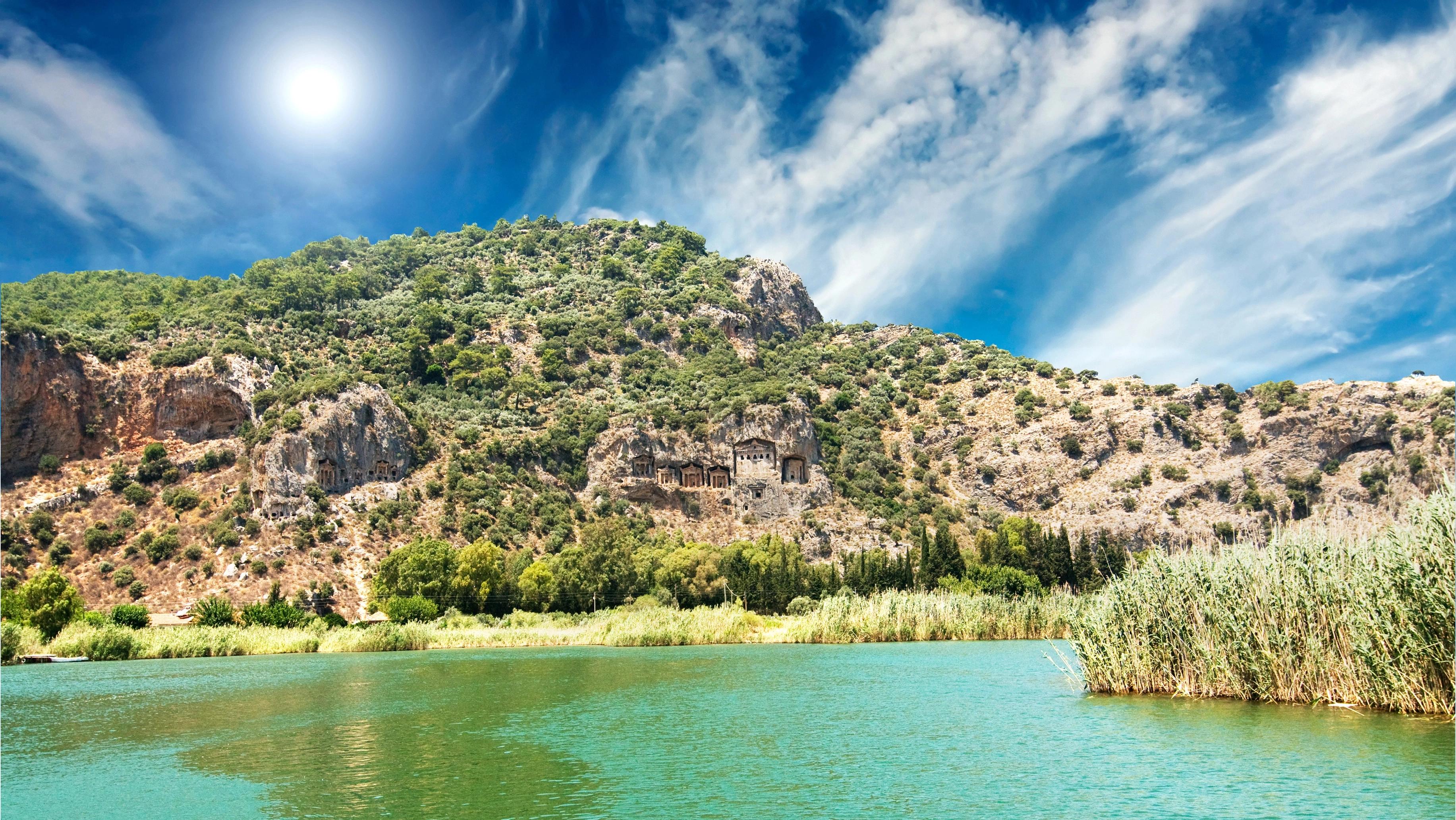 Výhled na jezero s tyrkysovou vodou, zeleným porostem a skalnatými kopci pod modrou oblohou