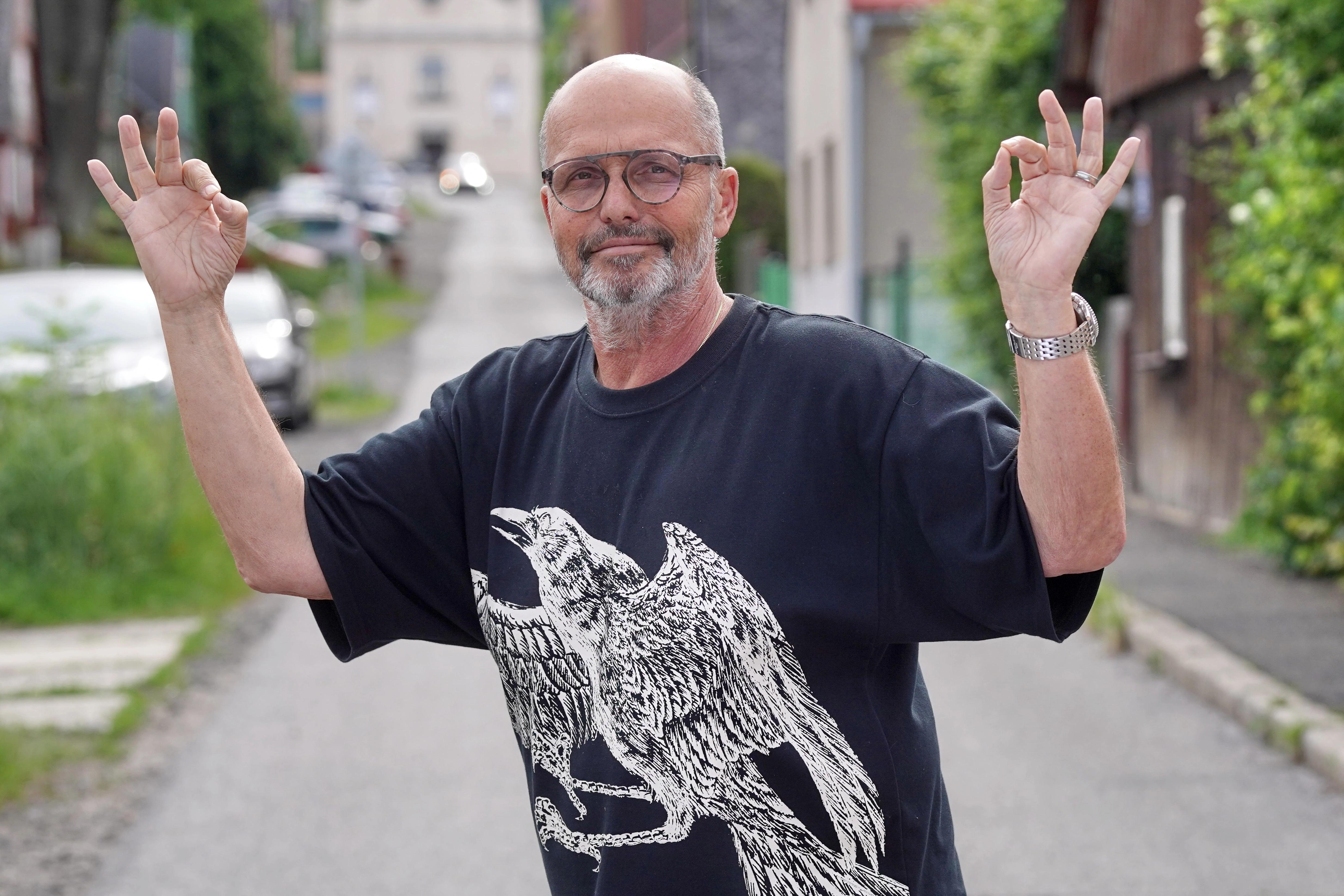 Zdeněk Pohlreich v tričku s orlem během rozhovoru, v pozadí motorky