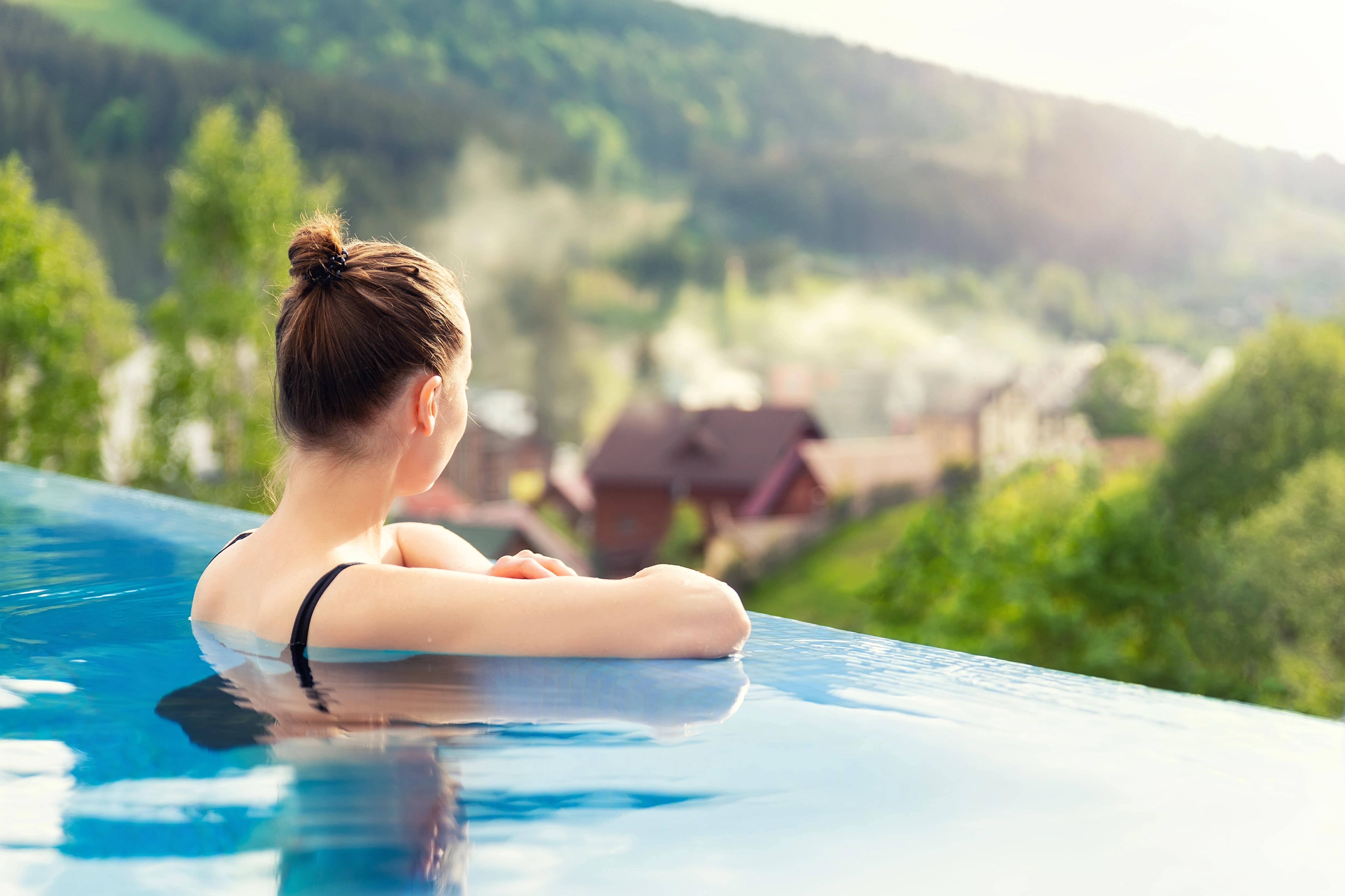 Žena relaxující v nekonečném bazénu s výhledem na přírodu.