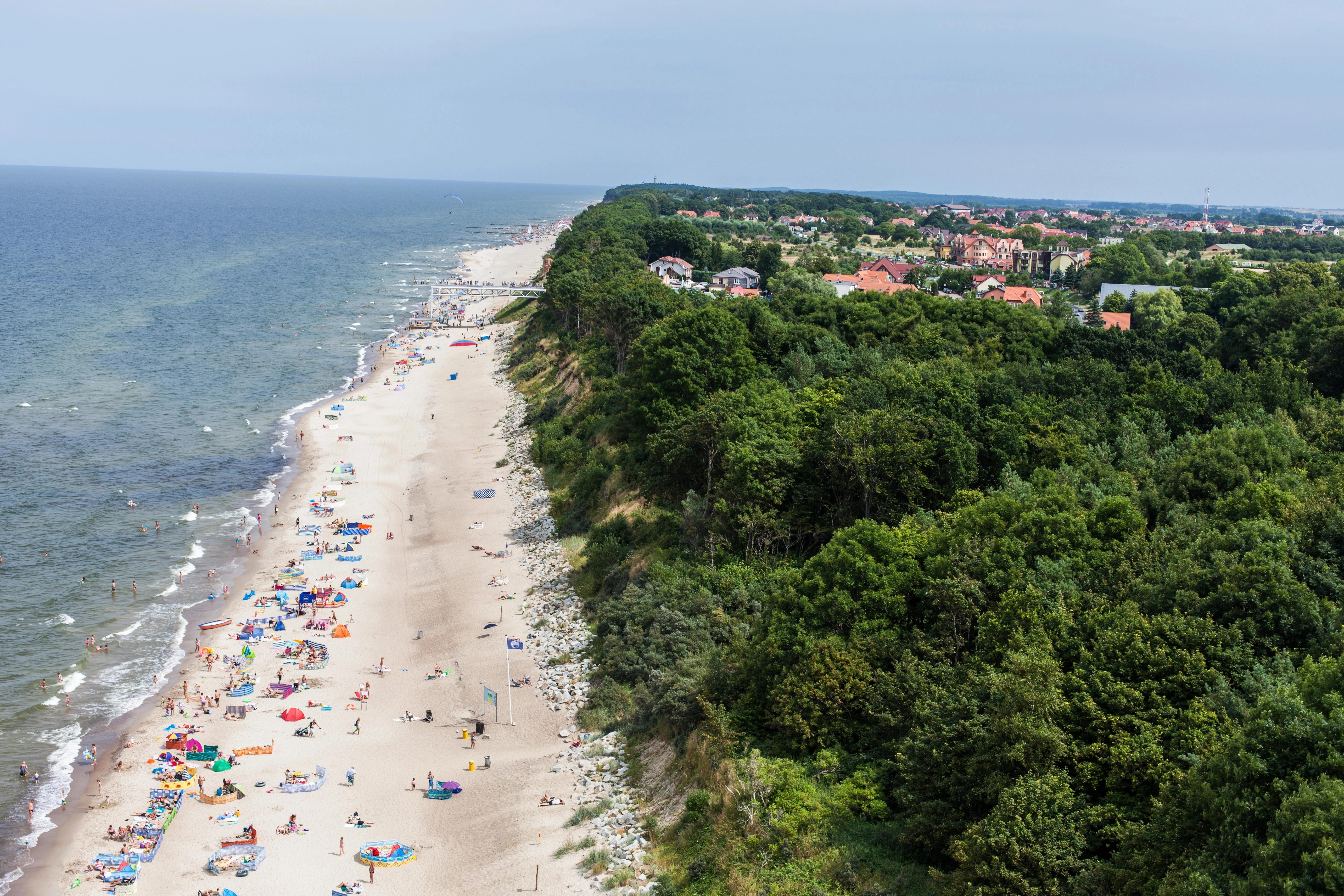 Letecký pohled na pláž s turisty a lesem v pozadí,