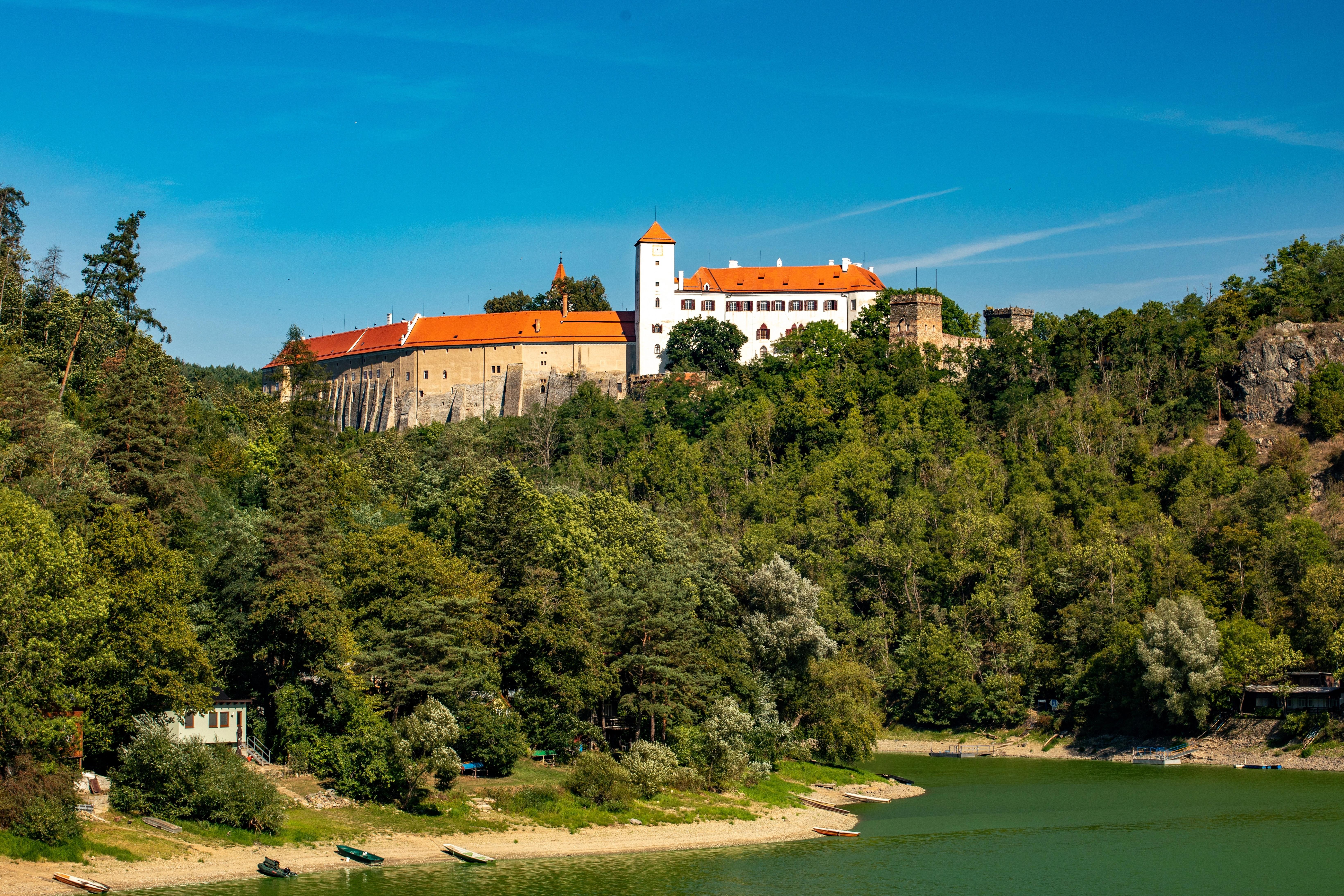 Historický zámek s červenou střechou nad řekou.