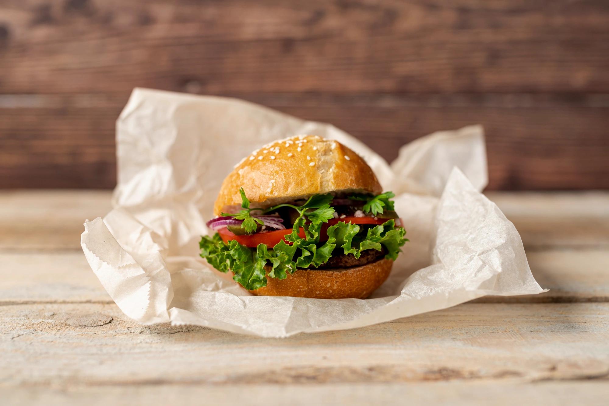 Tři různé burgery položené vedle sebe na dřevěném prkénku