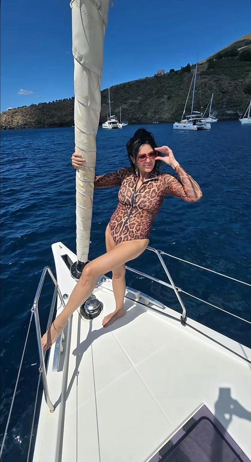 Ilona Csáková sedí v plavkách na přídi jachty, v pozadí moře a plachetnice