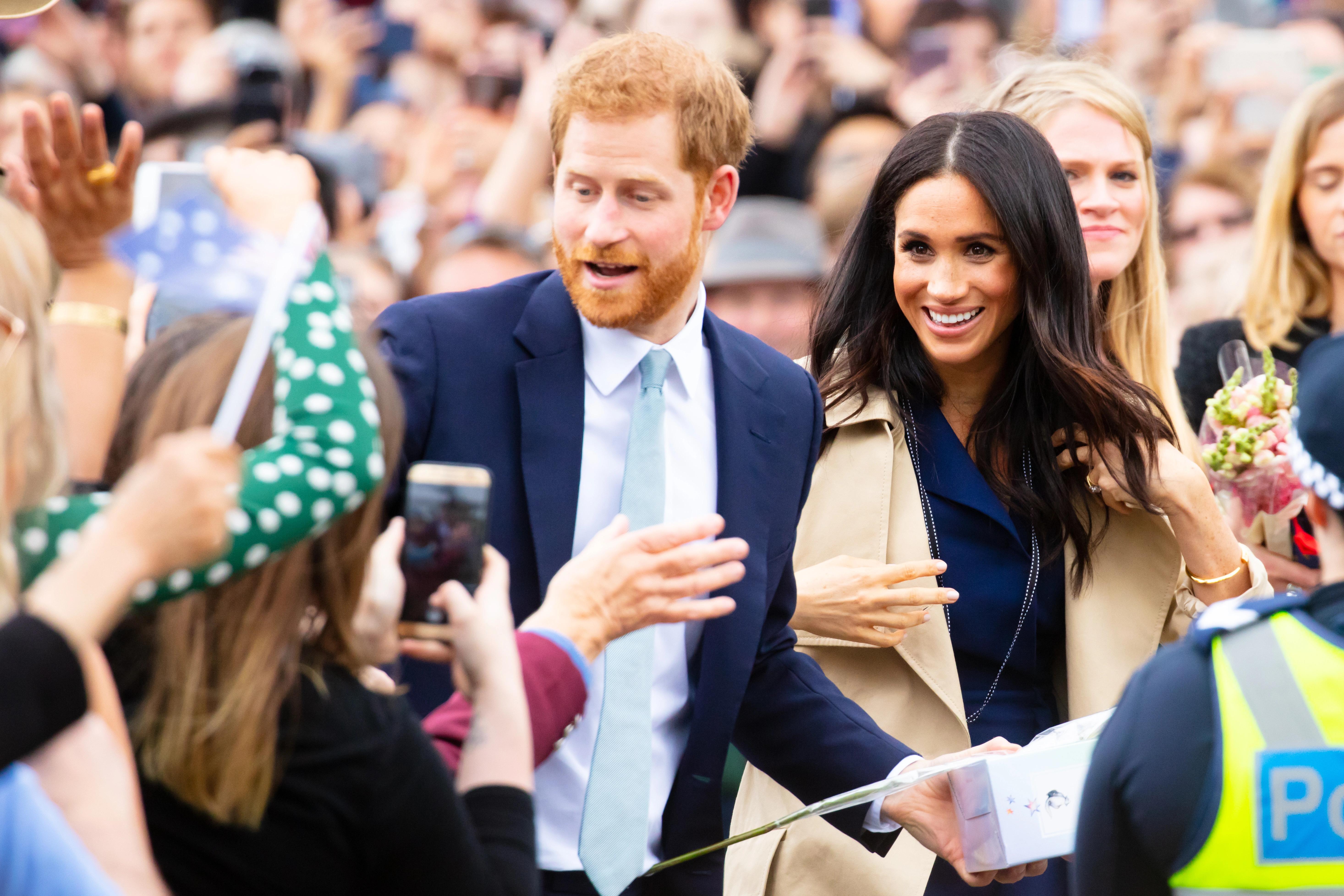 Princ Harry a Meghan Markle se usmívají a zdraví lidi při veřejné akci