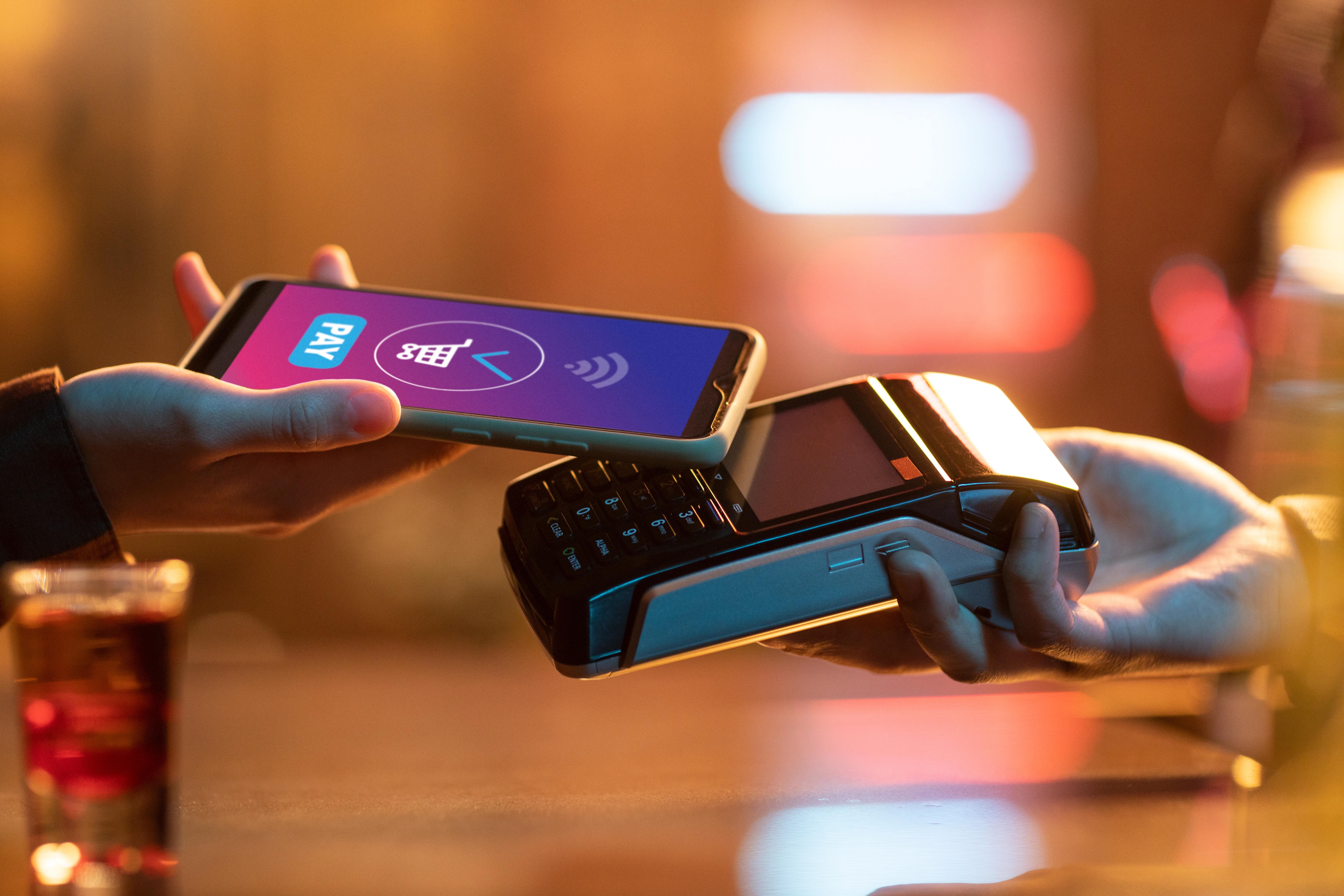 Ruka držící mobil s otevřenou platební aplikací před terminálem