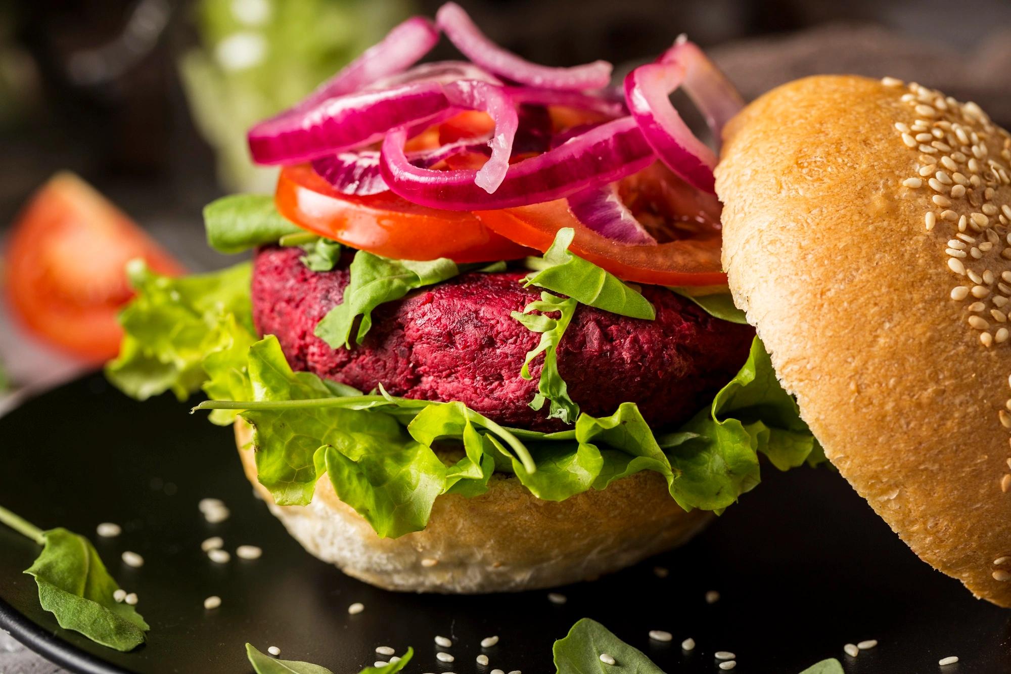 Ruka držící hamburger s rozkrojenou houskou a masem