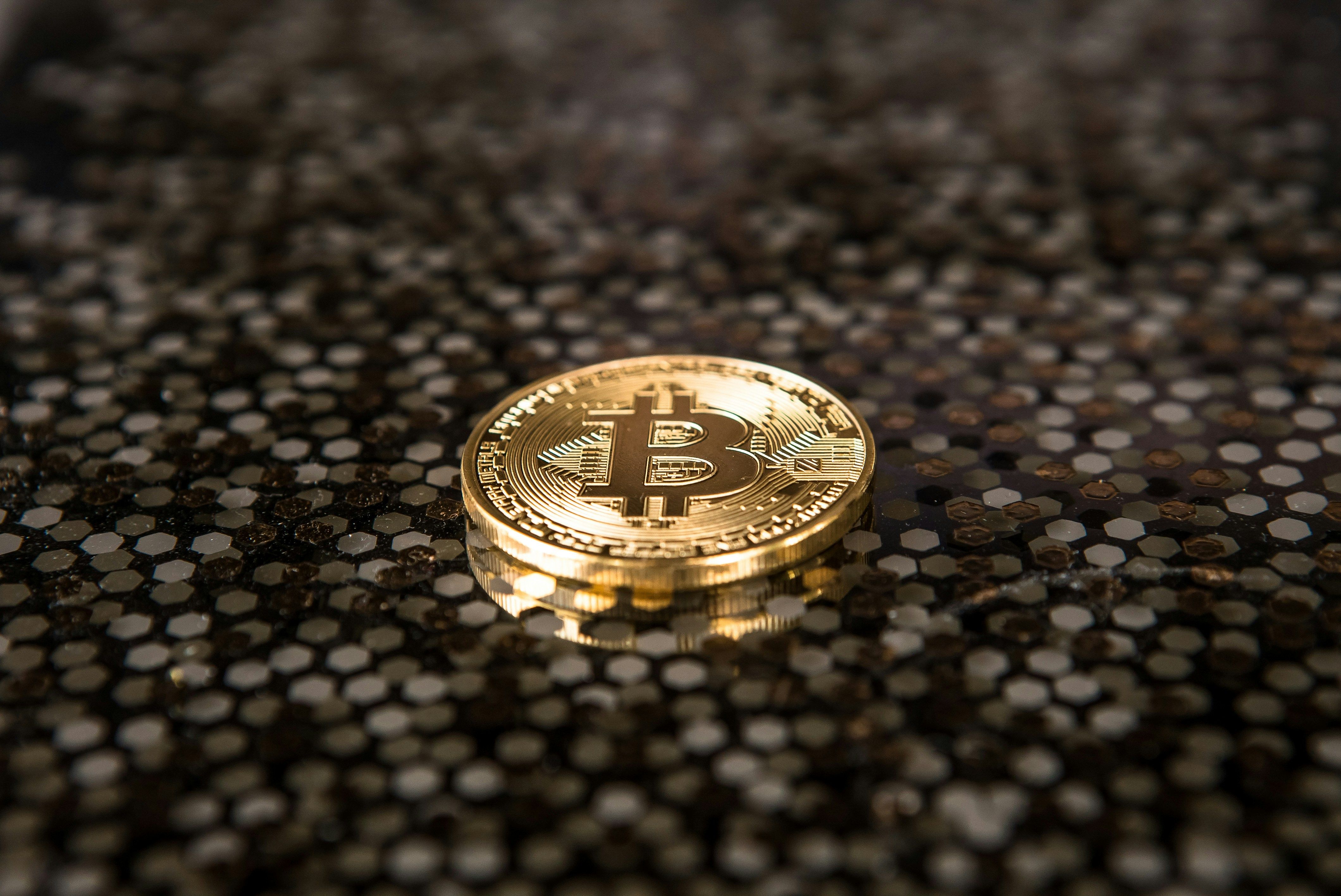 Zlatá mince s logem Bitcoinu položená na třpytivém pozadí.