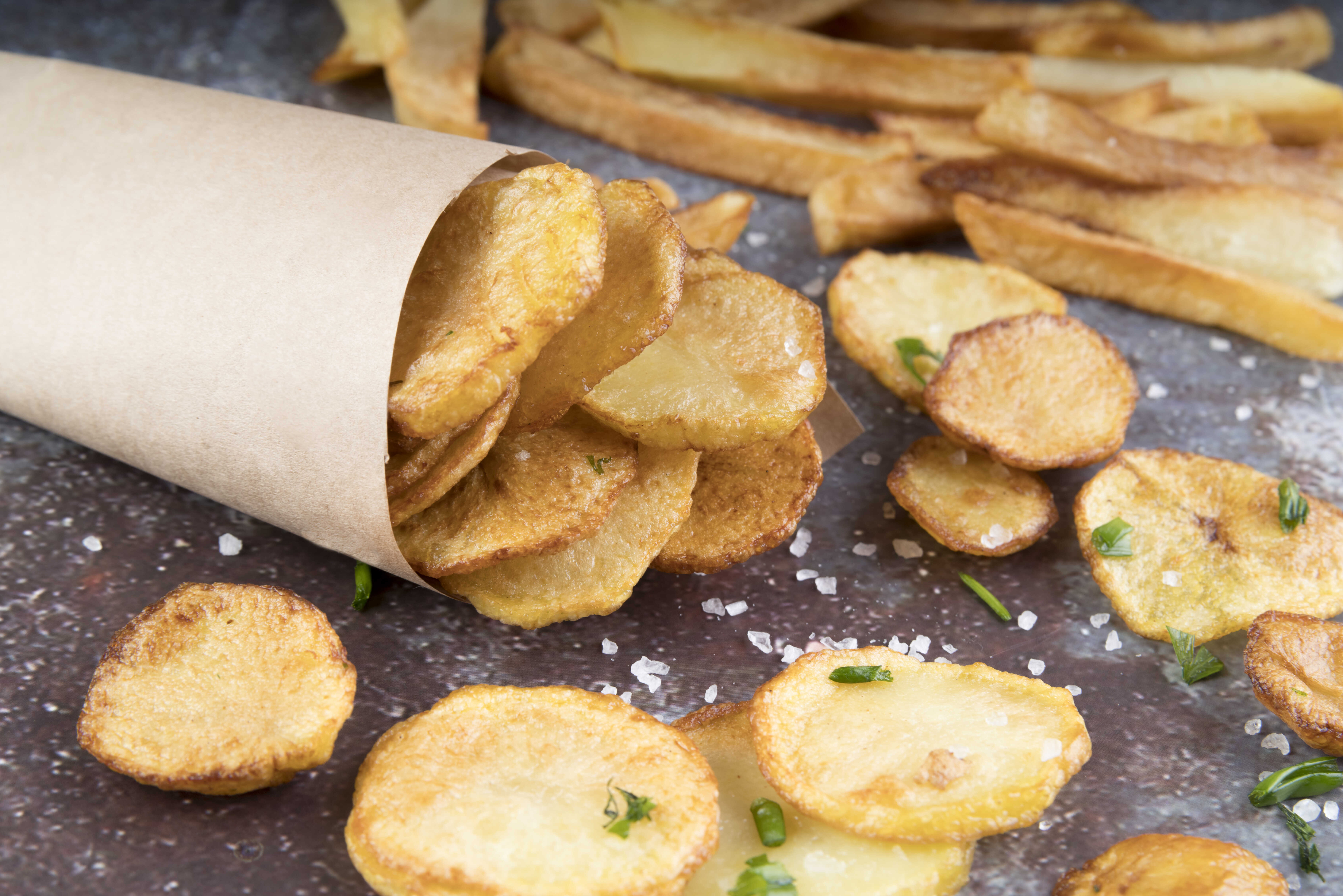 Křupavé chipsy z bramborových slupek servírované na stole, posypané solí a nasekanou pažitkou