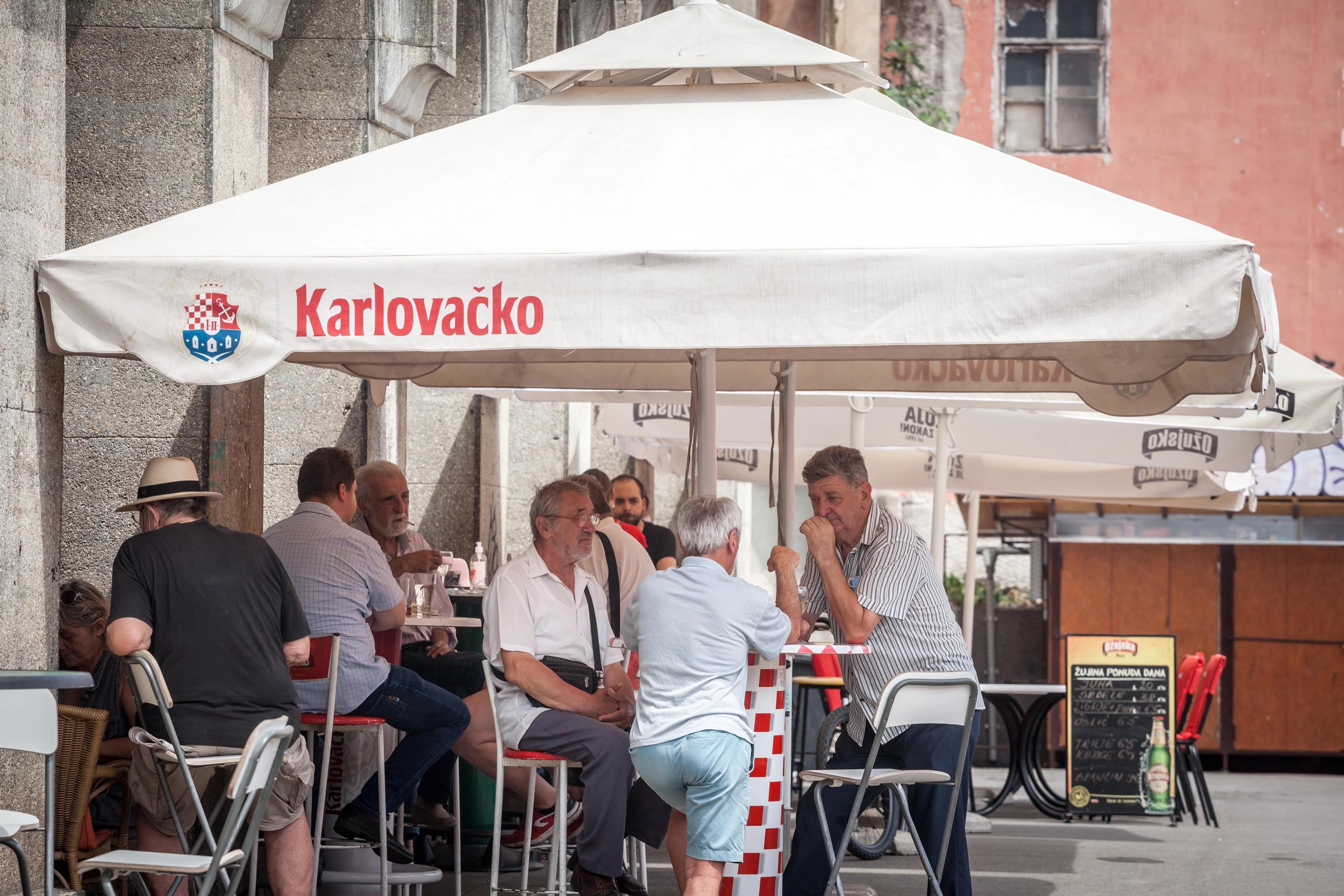 Hosté sedí u stolů před kavárnou v Chorvatsku.