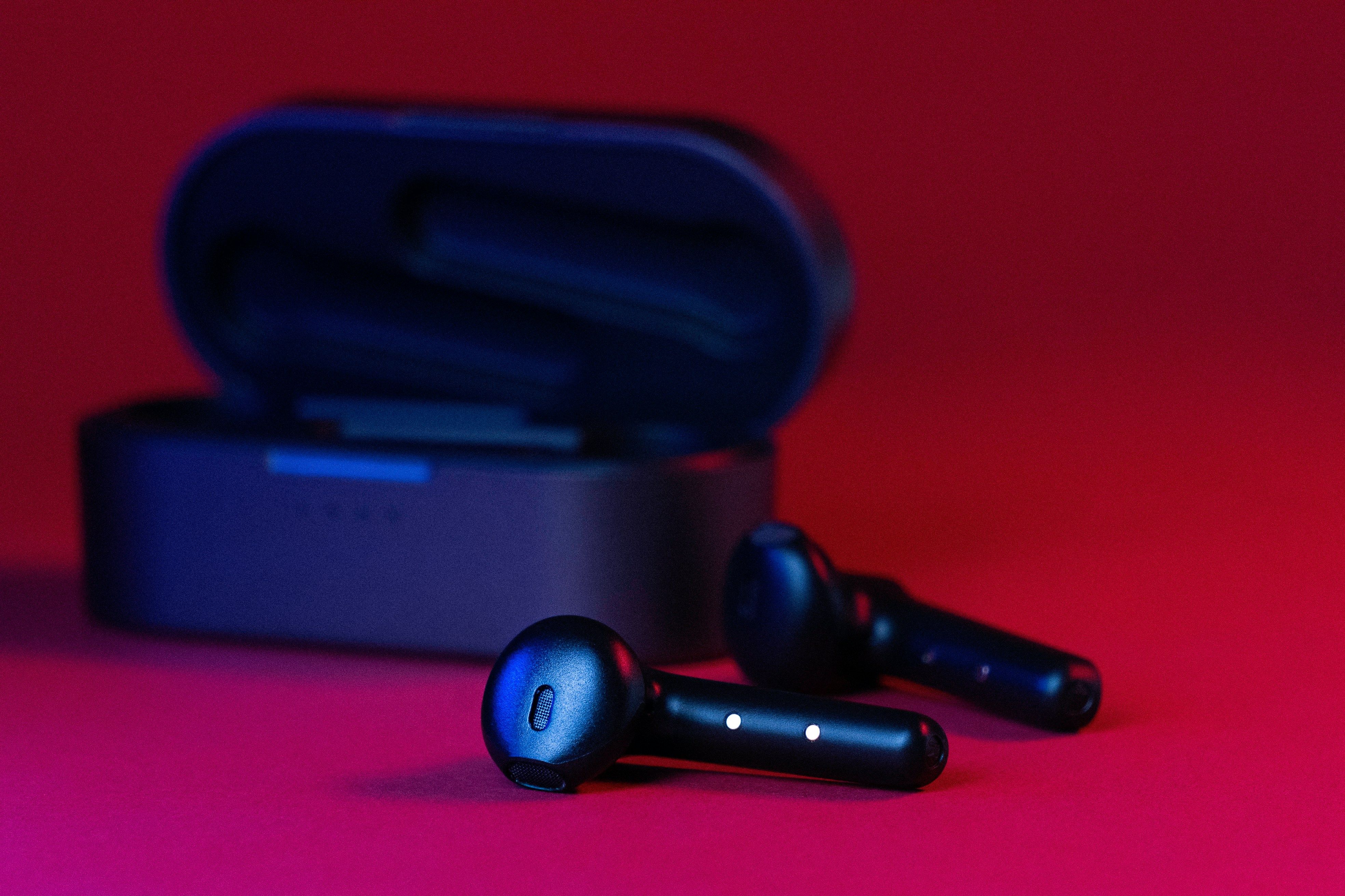 Černá bezdrátová sluchátka True Wireless s otevřeným pouzdrem na červeném pozadí
