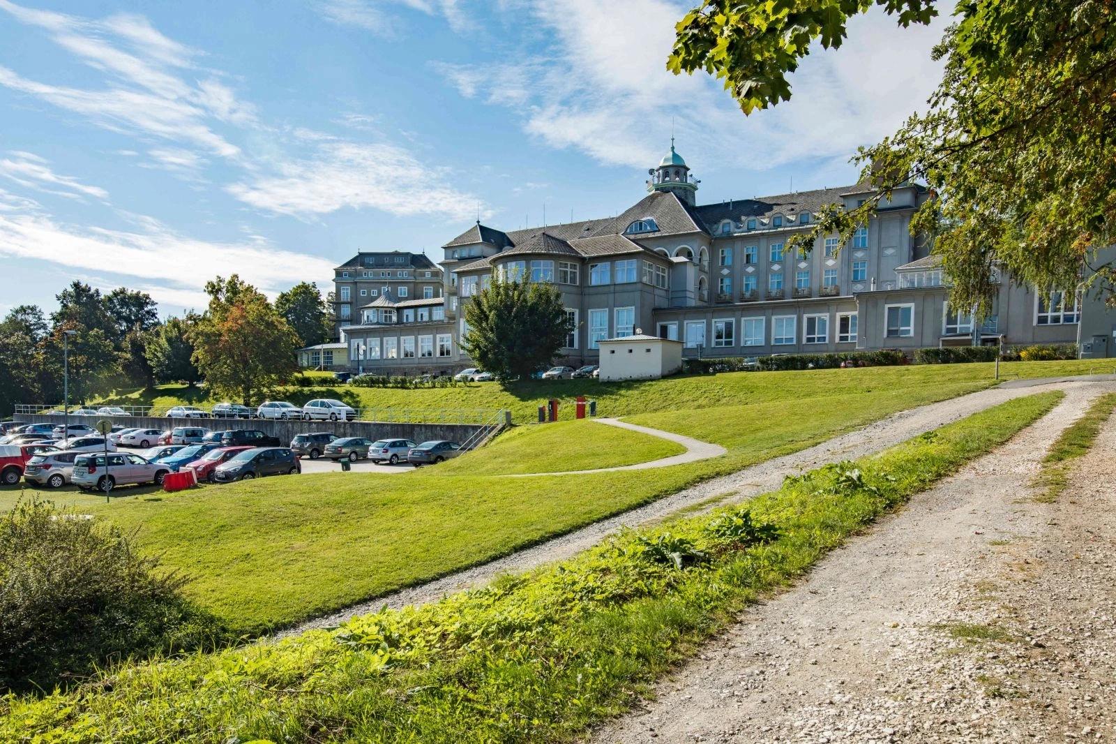 Historická lázeňská budova s věžičkou a parkovištěm v popředí